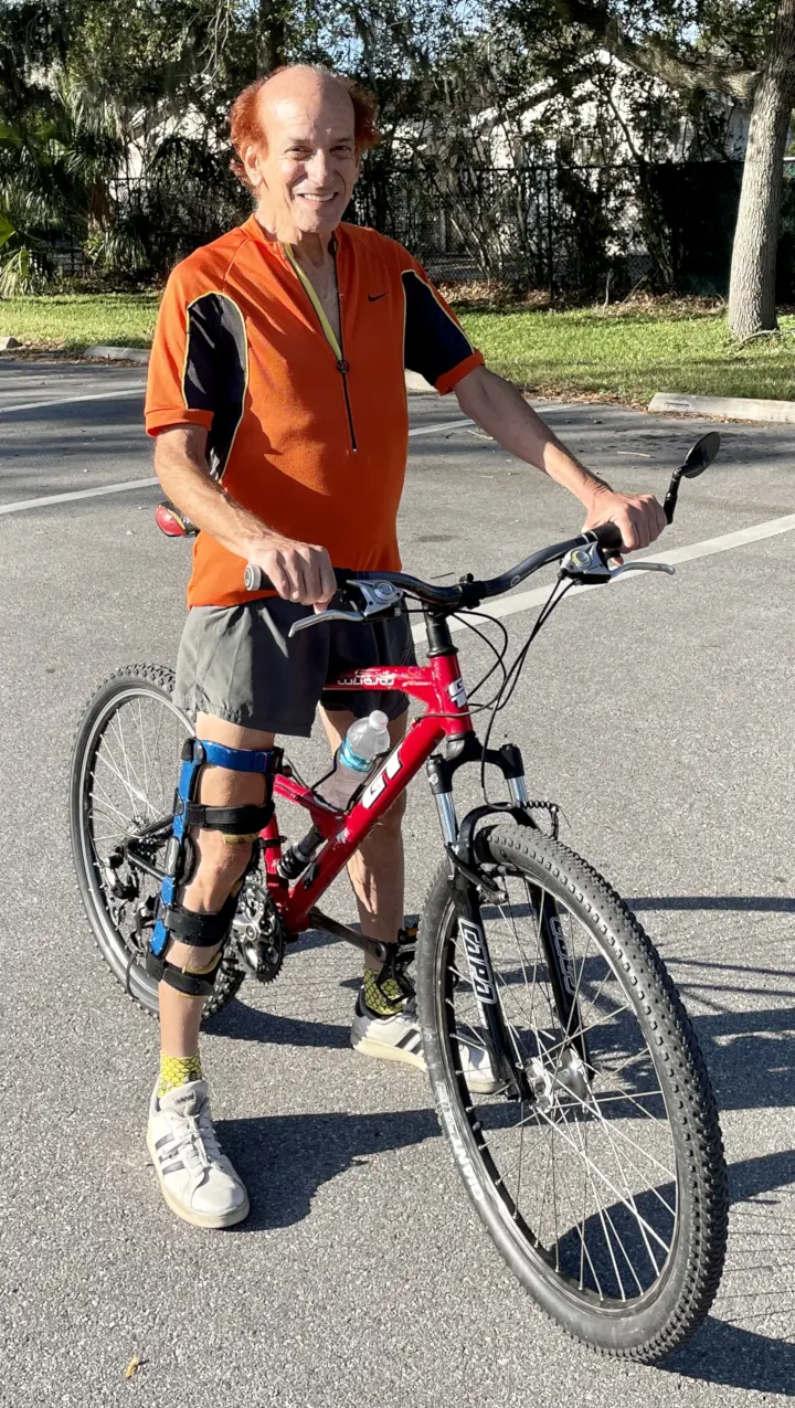 Mitchell D. Miller riding a red GT RTS-3 bicycle across a pedestrian bridge at Raymond H. Neri Park, St. Petersburg, Florida. Wearing a red jersey and blue knee brace, smiling on a partly cloudy day.